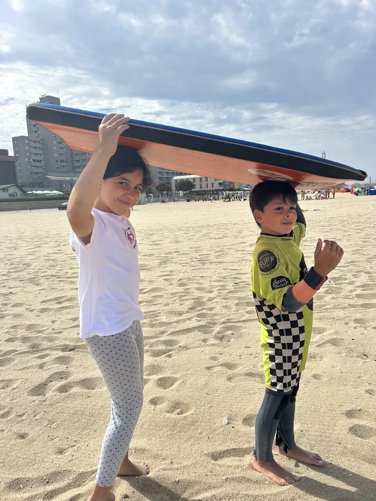 Duas crianças a transportar a prancha na praia