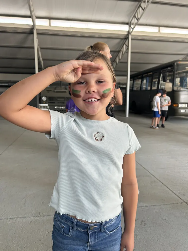 Menina em continência, com pintura de camuflagem